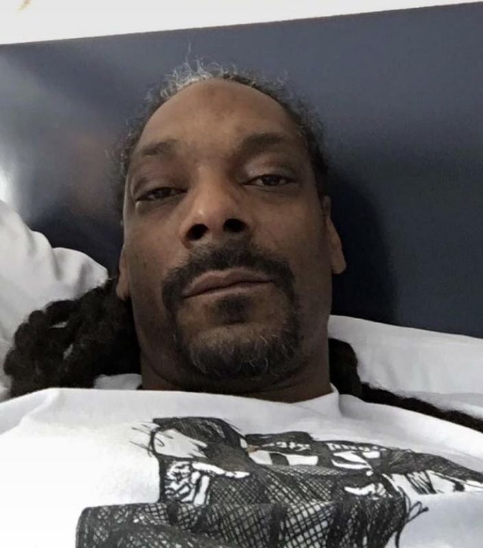 Close crop of Snoop Dogg's selfie wearing a white illustrated graphic T-shirt.
