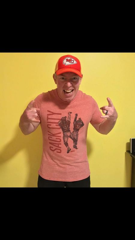 A Kansas City Chiefs fan in a Chiefs cap flexing in a red 500 Level 'Sack City' T-shirt featuring Tamba Hali and Justin Houston.